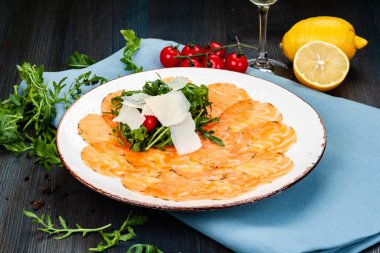 Arugula yapraklı somon carpaccio, parmesan peyniri ve beyaz tabakta vişneli domates..