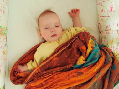 Bebek yatakta sırt üstü uyuyor.