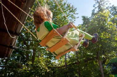 Açık yeşil elbiseli çocuk salıncakta sallanıyor.