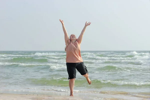 Contented girl is jumping on the beach against the background of
