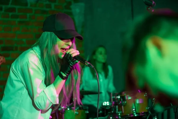 キャップの若い可愛い女の子がロッククラブで歌ってる ナイトクラブの若い音楽バンド 魂のための音楽 — ストック写真