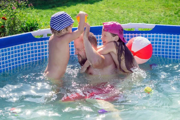 Bir baba, çocuklarıyla birlikte önceden üretilmiş bir havuzda eğlenir. Aile oyunları temiz havada suda..