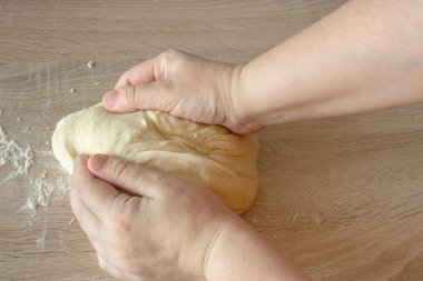 Ahşap bir masada hamur yoğurmak için hamur yoğurup un serpiştiren bir aşçının elindeki üst manzara..