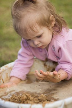 Küçük kız evin avlusundaki bir havuzda hevesle çamurla oynuyor. Çocuk banyoda kum ve su karışımını yoğurur..