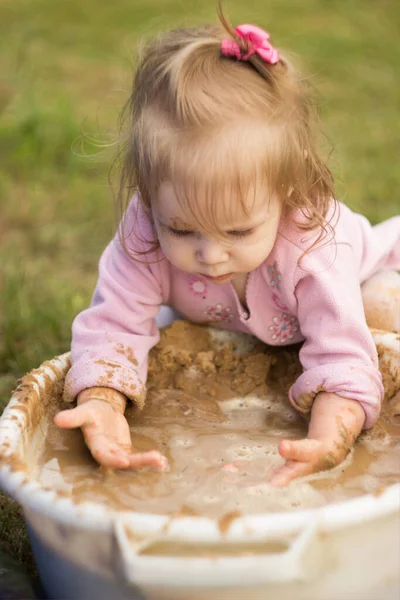 小女孩热切地在房子院子里的一个盆子里玩泥巴 孩子们在浴室里把沙子和水揉合在一起 — 图库照片