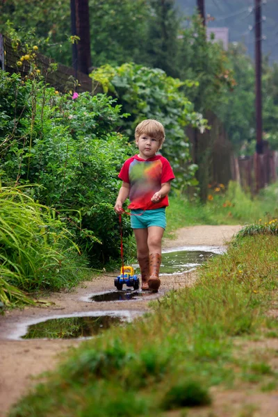 Een Jongetje Met Rubberen Laarzen Trekt Aan Een Speelgoedauto Tractor — Stockfoto