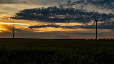 Rüzgar jeneratörü gün batımında çimen tarlasında bulutlarla