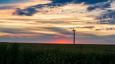 Rüzgar jeneratörü gün batımında çimen tarlasında bulutlarla