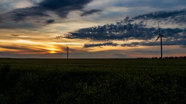 Rüzgar jeneratörü gün batımında çimen tarlasında bulutlarla
