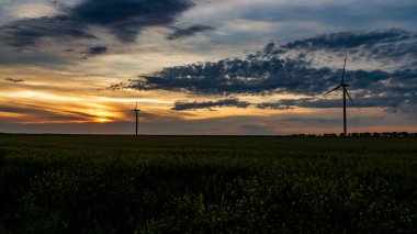 Rüzgar jeneratörü gün batımında çimen tarlasında bulutlarla
