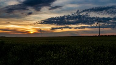 Rüzgar jeneratörü gün batımında çimen tarlasında bulutlarla