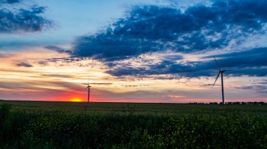 Rüzgar jeneratörü gün batımında çimen tarlasında bulutlarla