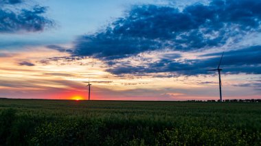 Rüzgar jeneratörü gün batımında çimen tarlasında bulutlarla