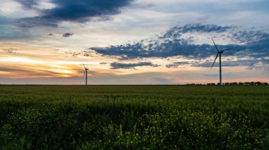 Rüzgar jeneratörü gün batımında çimen tarlasında bulutlarla