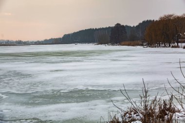 Ormanın arka planında, güneşin günbatımında donmuş donmuş bir göl.