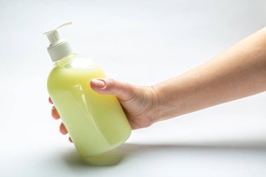 Kadın eli beyaz zemin üzerinde sıvı sarı sabun bulunan bir şişe tutuyor. Yatay oryantasyon. Yüksek kalite fotoğraf
