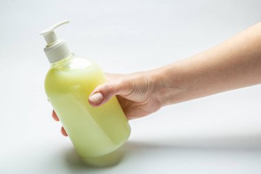 Kadın eli beyaz arka planda üzerinde sıvı sarı antiseptik sabun bulunan bir şişe tutuyor. Yatay oryantasyon. Yüksek kalite fotoğraf
