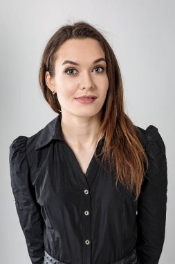 Siyah elbiseli, uzun saçlı esmer bir kız gizemli bir şekilde dilinin ucunu gösteriyor. Beyaz arka planda stüdyo portresi. Dikey yönelim.