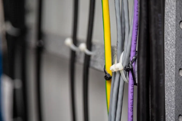 Cables fastened with white ties on the cable ladder. Black, gray, yellow, purple wires. Cable management. Close-up. Horizontal orientation.