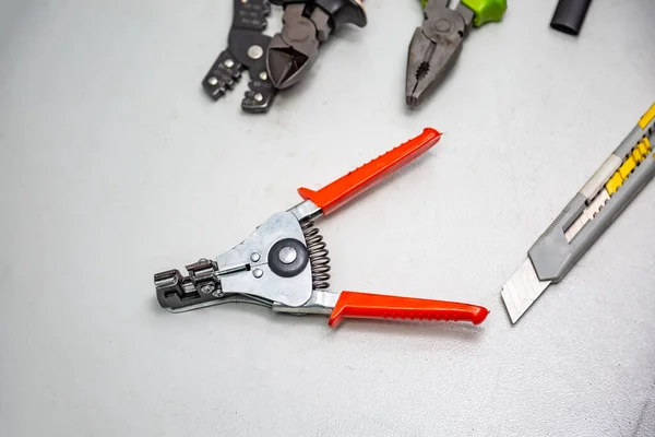 Tools for electrical installation on a white background. In the foreground a stripper for stripping wires. Tool for crimping wires, pliers, wire cutters, segment knife. Horizontal orientation.