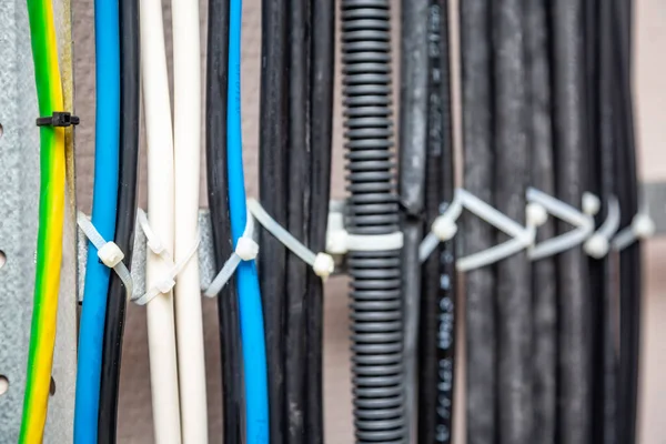 Cables fastened with white ties on the cable ladder. Black, gray, yellow, white, ground wires, corrugated cable. Cable management. Close-up. Horizontal orientation.