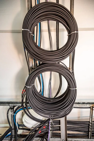 Управление кабелем. Рабочие провода, кабели, вкрученные в катушку, круг. Два кольца скрученных проводов, каток проволоки на стене. Вертикальная ориентация . — стоковое фото