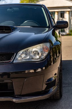 Güneşli bir günde siyah araba parazitli. Arabanın ön tarafı, kaput, far ve tekerlek. Dikey yönelim.