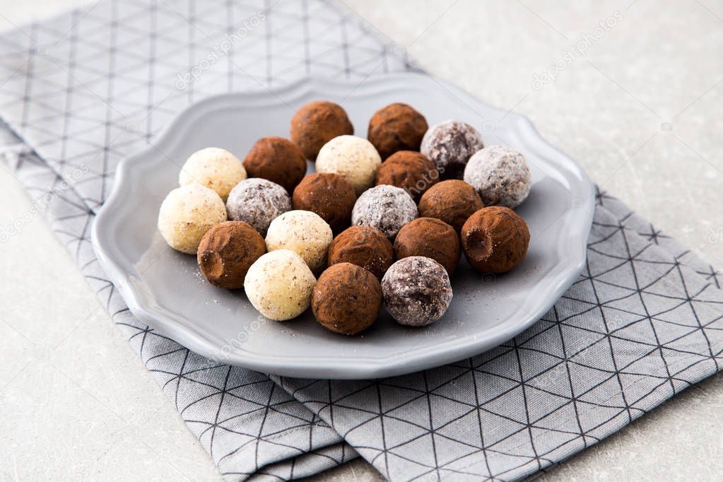 Assorted chocolate truffles with cocoa powder, coconut and chopped hazelnuts on a dessert plate