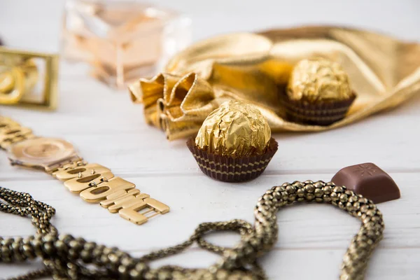 Set di accessori e dolci da donna in colore dorato su fondo legno: profumo, caramelle, cioccolato, orologio, gioielli, borsa dorata. Copia space.selective fuoco . — Foto Stock