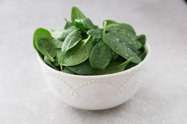 Mini spinaci freschi lavati in un piatto su uno sfondo di pietra — Foto Stock