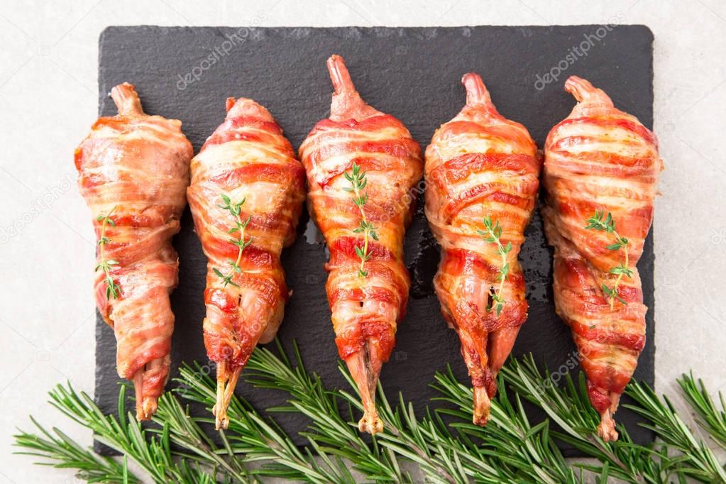 baked quail wrapped in bacon on a slate board with spices