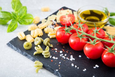 Makarna malzemeler. Kiraz domates, makarna, taze fesleğen, baharat taş bir arka plan üzerinde