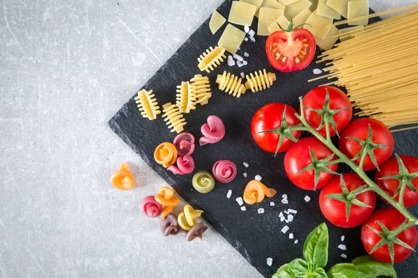 Makarna malzemeler. Kiraz domates, makarna, taze fesleğen, baharat taş bir arka plan üzerinde