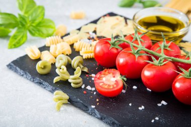 Makarna malzemeler. Kiraz domates, makarna, taze fesleğen, baharat taş bir arka plan üzerinde