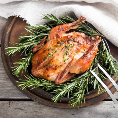 Bitkilerle doğal ahşap arka plan üzerinde kızarmış bütün tavuk. Kim