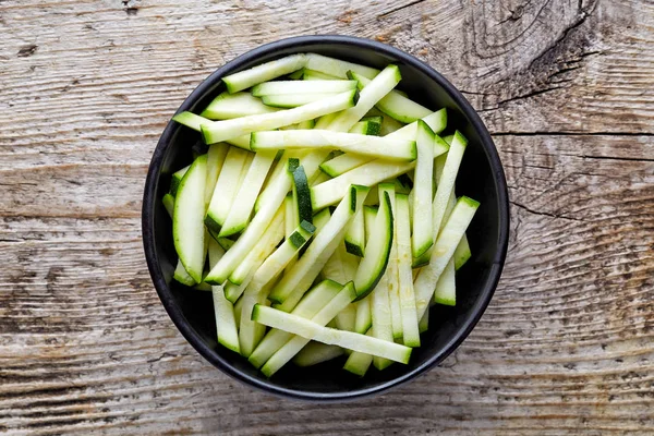 Bowl of zucchini slices on wooden table, from above — Stock Photo, Image