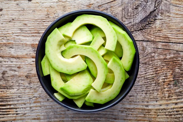 Bowl of avocado slices on wooden table, from above — Stock Photo, Image