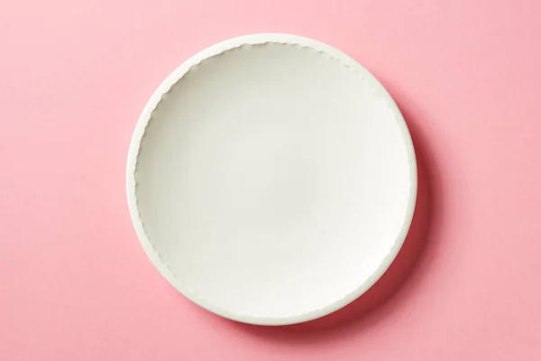 Біла тарілка на рожевому фоні, зверху — стокове фото