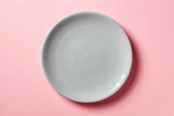 Сіра тарілка на рожевому фоні, зверху — стокове фото