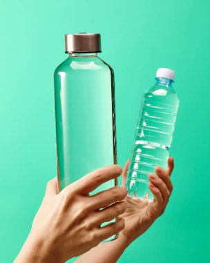 Sıfır atık kavramı - yeniden kullanılabilir cam su şişesine karşı tek kullanımlık nane yeşili arka planda plastik şişe