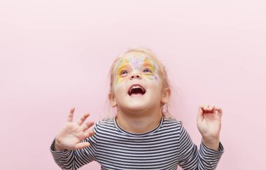 Pembe arka planda parlak bir yüz resmi olan, 3 yaşında, güzel, gülümseyen, küçük bir kız çocuğu. Eğlenceli duygular, mutlu çocukluk