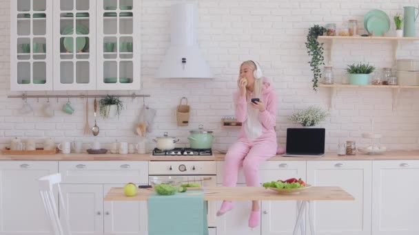 Hezká dívka na sobě růžová kigurumi sedí na kuchyňské sadě — Stock video