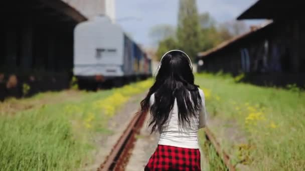 Brunette puts on white wireless headphones dances on rails — Stock Video