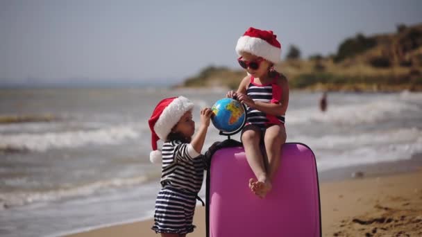 Grappige meisjes in Santa hoeden spelen met globe per geval op zand — Stockvideo