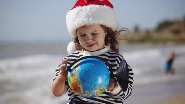 Concentrated girl in red Christmas hat examines globe — Stock Video