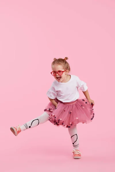 快乐的童年 滑稽的小女孩穿着郁金香裙跳跃着 在粉红色的背景下享受着孤独的快乐 庆祝一个充满活力的嘉年华为孩子 生日派对 真正的感情 案文的篇幅 — 图库照片