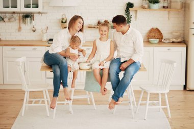 Mutfakta kahvaltı hazırlayan mutlu beyaz aile. İki küçük çocuklu ebeveynler yemek masasında oturmuş eğleniyorlar..