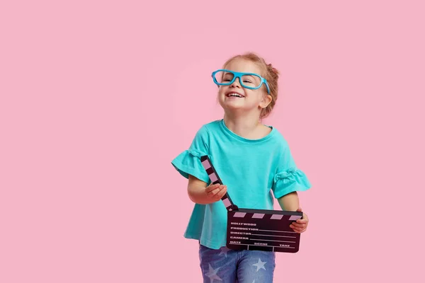 戴著电影眼镜的笑容可亲的小女孩拿着电影胶片 用粉红的背景把拍板隔开 工作室肖像 童年生活方式概念 Tex的复制空间 — 图库照片