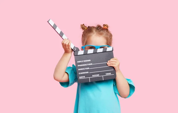 Sinema gözlüklü komik gülümseyen kız elinde pembe arka planda izole edilmiş bir film şeridi tutuyor. Stüdyo portresi. Çocukluk yaşam tarzı konsepti. Tex için alanı kopyala