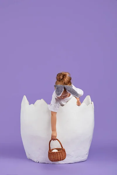 衣装の幸せな子供の女の子耳と卵とバスケットとイースターウサギのウサギ 紫の背景に大きな鶏の卵の女の子 — ストック写真